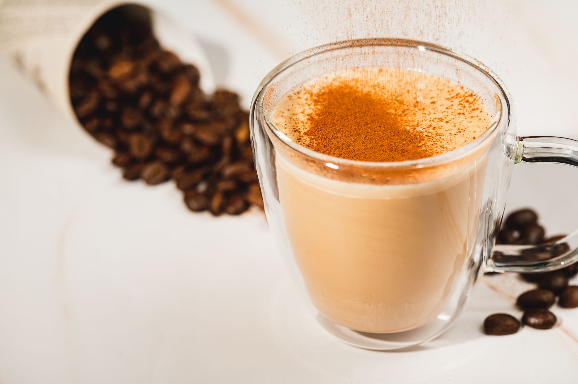 A glass cup of cinnamon latte dusted with ground cinnamon, with coffee beans beside it