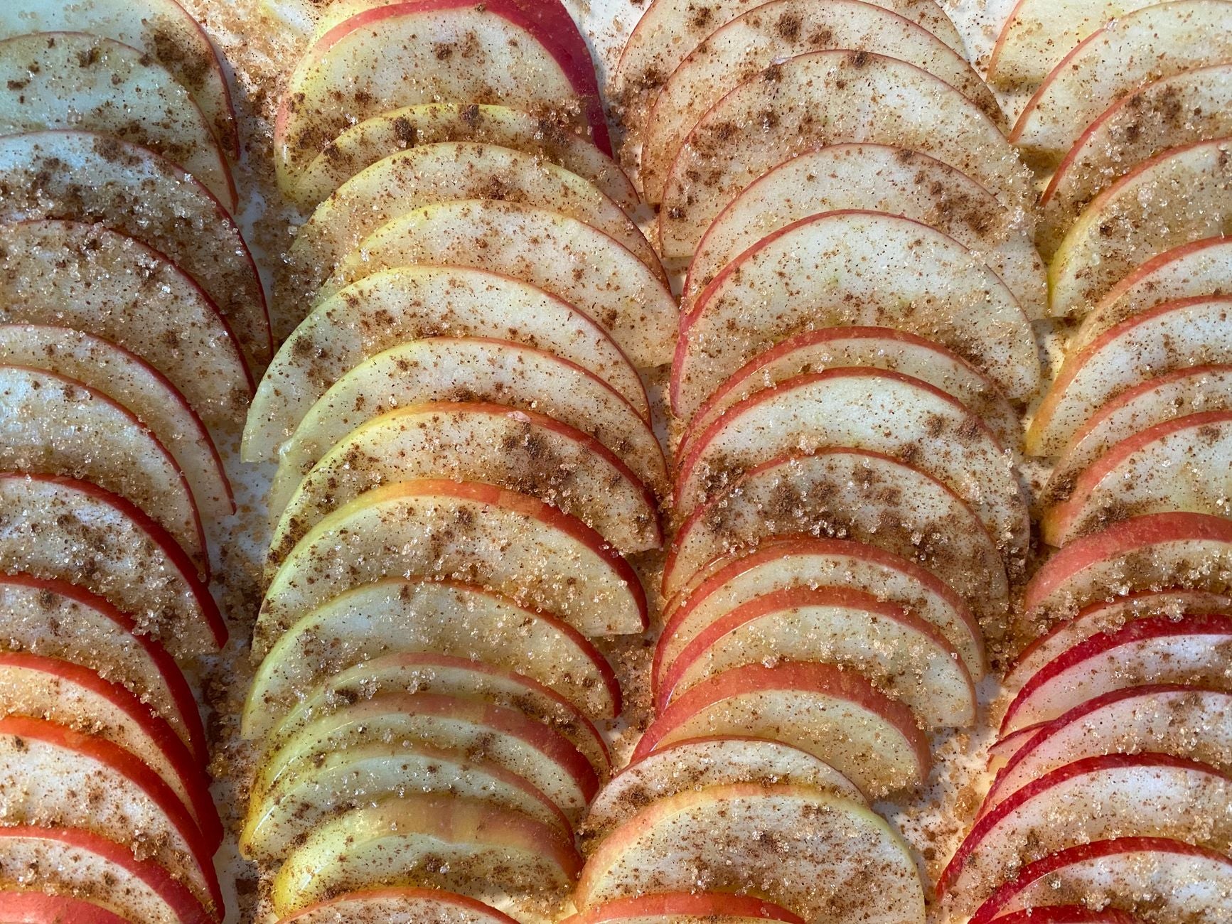 Rows of thinly sliced apples dusted with cinnamon and sugar, ready to bake into an apple crisp