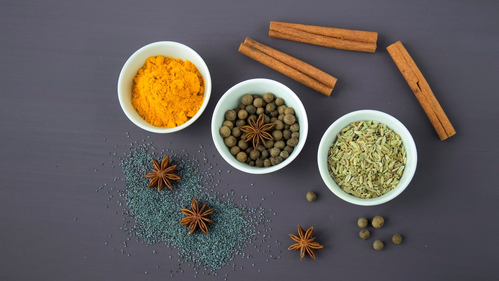 An overhead arrangement of whole and ground spices, including turmeric, cinnamon and peppercorns