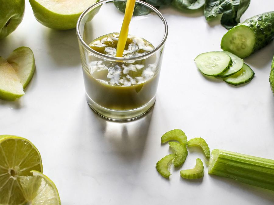 A green juice poured beside spinach, lime and cucumber